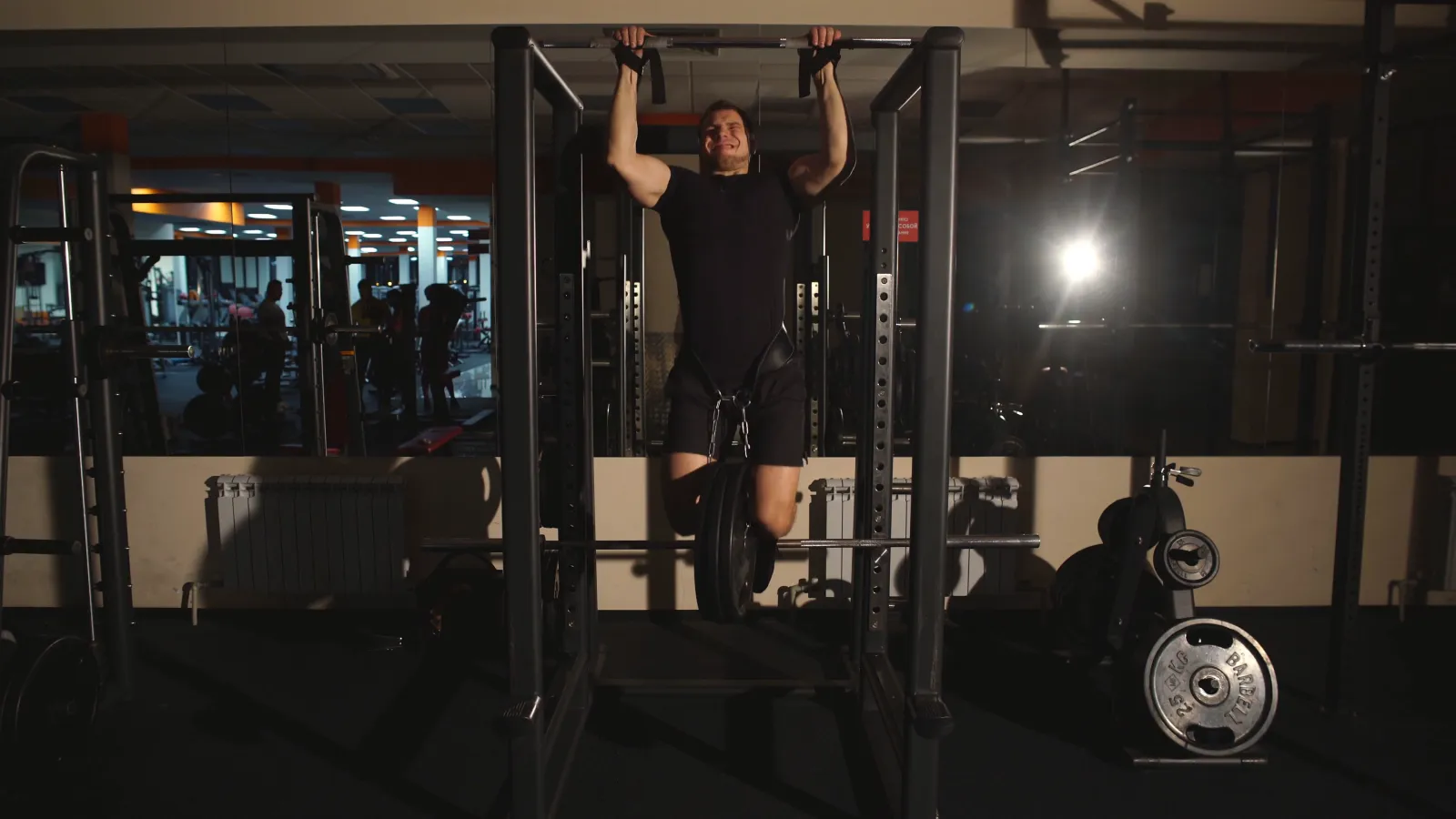 A man doing pull-ups on a bar in a dark gym