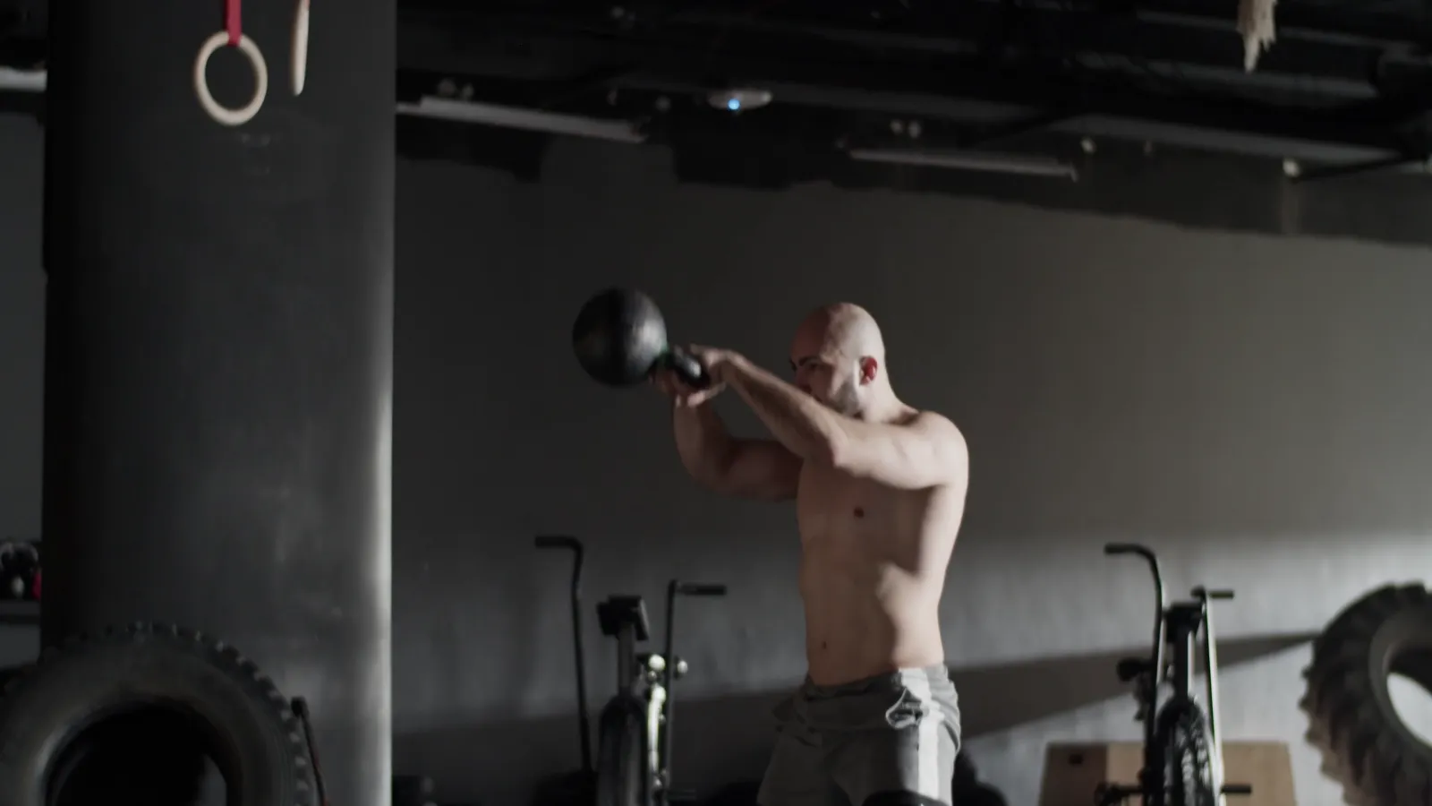 A man swinging a kettlebell to chest height in a dim gym, the top of a two-hand swing