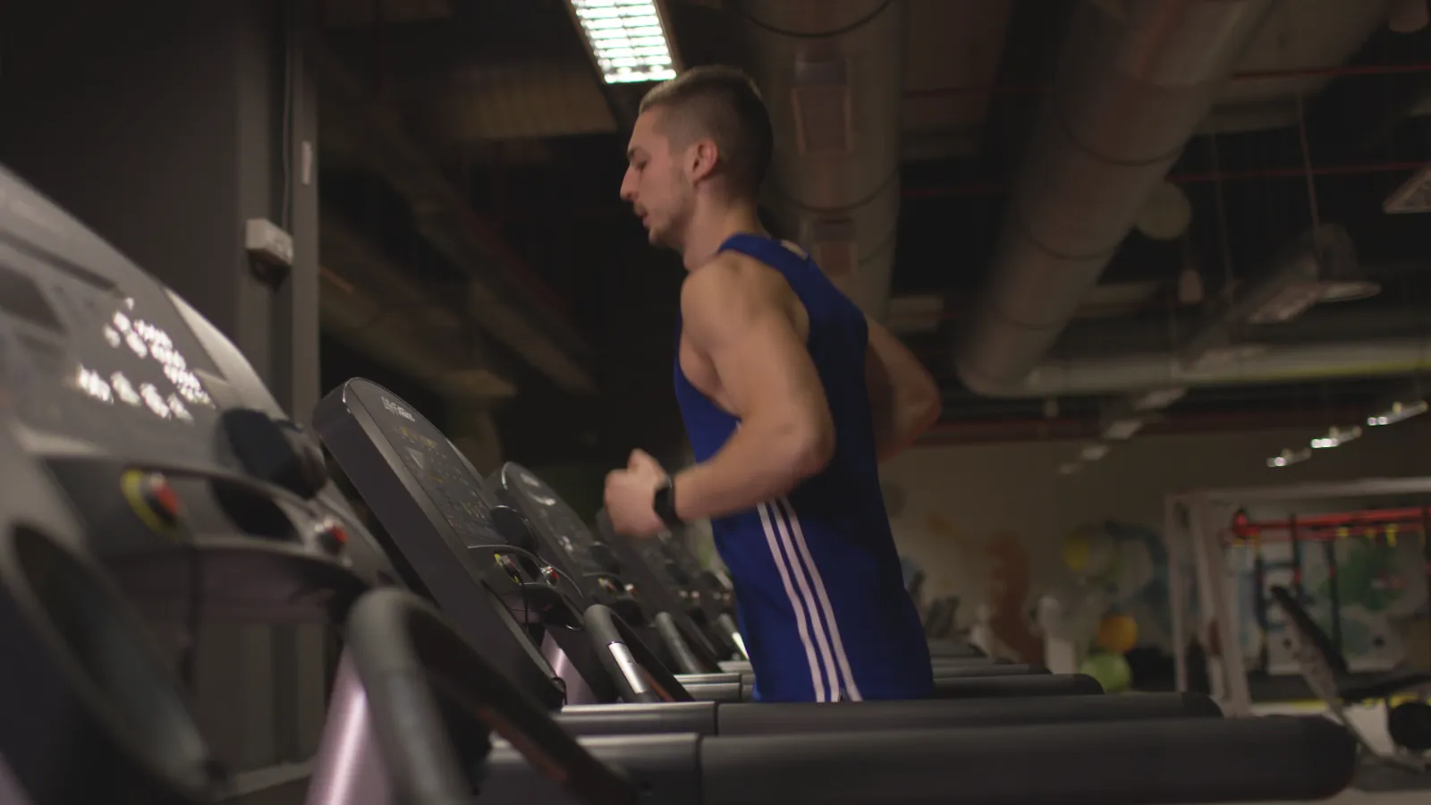 A runner mid-stride on a treadmill in a dark gym